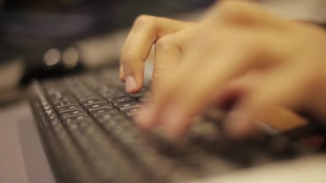 Close up of human hands typing of a desktop PC keyboard at midnight or late night.