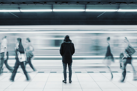 Long exposure of lonely man at subway station with blurry train and walking people