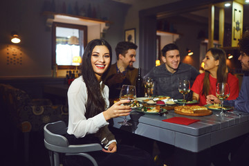 Woman with a glass against the background of friends in a restaurant.