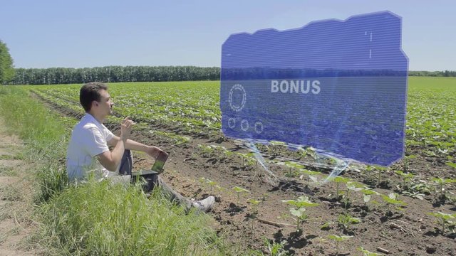 Man is working on HUD holographic display with text Bonus on the edge of the field. Businessman analyzes the situation on his plantation. Scientist examines future technology