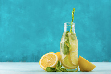 Fresh lemonade in glass bottle. Mint and lemon halves on blue fresh background