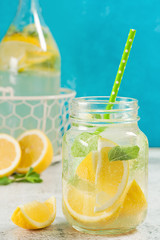 Fototapeta premium Fresh lemonade in mason jar. Mint and lemon halves on blue fresh background