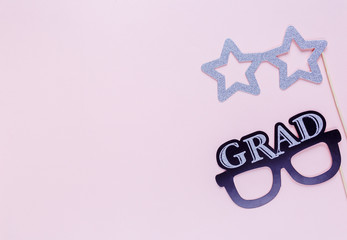 Creative background with photobooth props for graduation: hats, diploma, glasses, lips on pastel pink paper background. Education, study concept. 