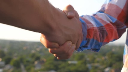 Two friends meeting on rooftop and greeting each other. Young men shaking hands on blurred cityscape background. Friendly handshake between guys outdoor. Concept of friendship. Close up Slow motion