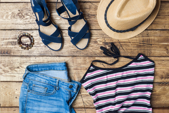 Summer women's clothes. Flat lay fashion photo. Blue jeans, t-shirt, sun hat, blue sandals on wooden background.