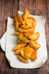 Fried potato wedges. Fast food. Chips served on paper and wooden background.
