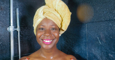 lifestyle portrait of young beautiful black afro American woman having a shower with her head wrapped in a towel smiling cheerful in hygiene and beauty concept