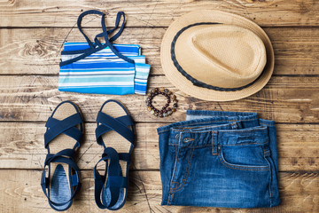 Summer women's clothes. Flat lay fashion photo. Blue jeans, t-shirt, sun hat, blue sandals on...