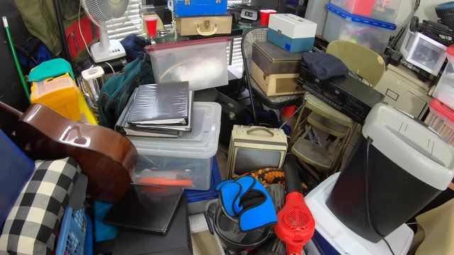 Cluttered hoarder room.  Slow dolly move over piles of household items, vintage electronics, business equipment and miscellaneous junk.