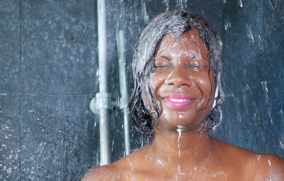 domestic lifestyle portrait of young happy and beautiful black afro American woman smiling happy taking a shower at home bathroom washing her hair with shampoo