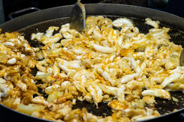 Fried squid eggs, a tasty Thai street food that simply calls attention of passing customers with its mouthwatering fragrance of seafood cooking on a hot pan, background blurred.