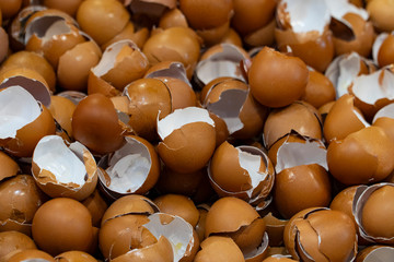 Eggshells at fresh food preparation make a large stack on a canteen table with background blurred.