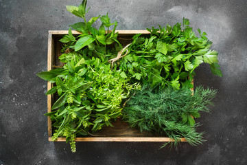 Fresh herbs, spice, parsley in wooden box on vintage black table.