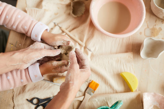 Top view closeup of mother and child shaping clay in pottery workshop for family, copy space