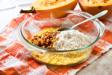 Raw washed millet, rice and raisins in a glass pan in the process of cooking milk pumpkin porridge