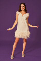 Naklejka premium Beautiful brunette woman in elegant cocktail white dress is posing in studio on purple background.
