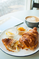 Fresh croissant with jam and butter and cappuccino with beautiful latte art on grey table in a cafe.