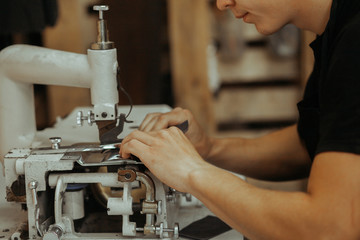 Close up of sewing machine working part with leather. The master's hands sews a leather product....