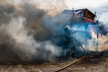 Firemen extinguishes a burning old wooden residential house. Firefighters at work on the fire. Fireman with a hose puts out the fire with water