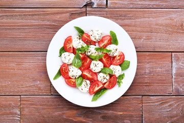 Mozzarella, tomatoes and basil leafs in plate on brown wooden table