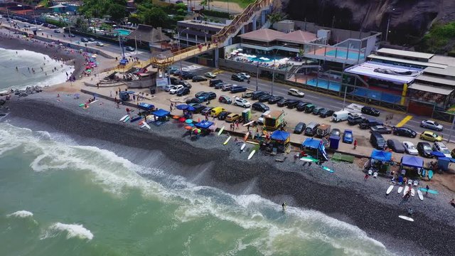 Drone aerial bird eye view of Makaha Beach shoreline. People relaxing at the beach, surf schools and group of surfers learning to surf in a bright summer day at Miraflores district, Lima, Peru.