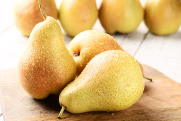 Ripe pears with water drops on brown cutting board
