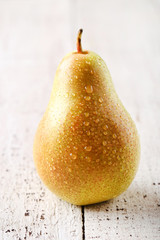 Ripe pear with water drops on white wooden table