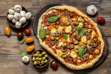pizza with mushrooms, tomatoes, olives and spinach and goat cheese on wooden background