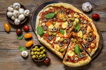 pizza with mushrooms, tomatoes, olives and spinach and goat cheese on wooden background
