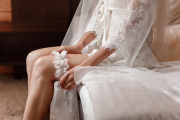 Woman wearing a garter on the leg. The bride holds in hand lose-up garter in hotel room. morning...