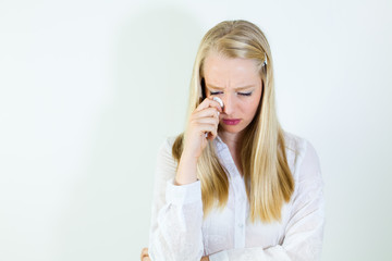 Sad,  young, blonde woman holding tissue, looking down.