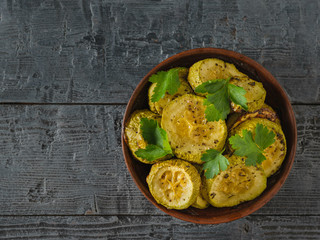 Baked zucchini slices in a clay bowl on a black wooden table. Vegetarian dish. Natural plant food. Flay lay.