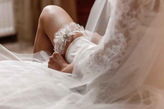 Woman wearing a garter on the leg. The bride holds in hand lose-up garter in hotel room. morning preparation wedding concept.