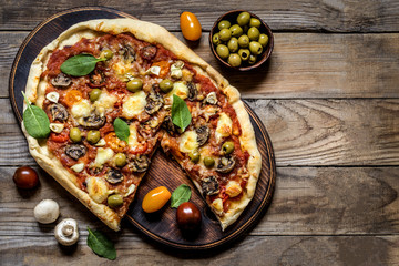 pizza with mushrooms, tomatoes, olives and spinach and goat cheese on wooden background