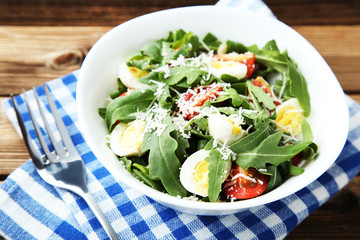 Salad with arugula leafs, tomatoes, eggs and fork on brown wooden table