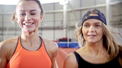 Two smiling athletic women friends running on a running track