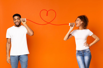 Young black couple with can phone on orange background
