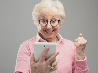 Happy surprised senior lady using a digital tablet