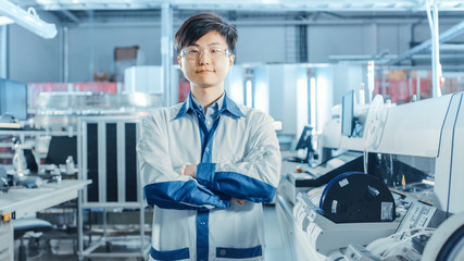 On High-Tech Factory: Portrait of Asian Worker with Crossed Arms. In the Background Electronic...