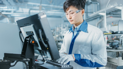 Fototapeta premium On High Tech Factory Asian Engineer Uses Computer for Programing Pick and Place Electronic Machinery for Printed Circuit Board Surface Mount Assembly Line. Production of PCB with SMT Machinery.