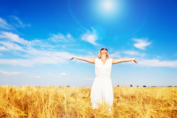 Happy, satisfied young woman with arms outstretched standing in the wheat field