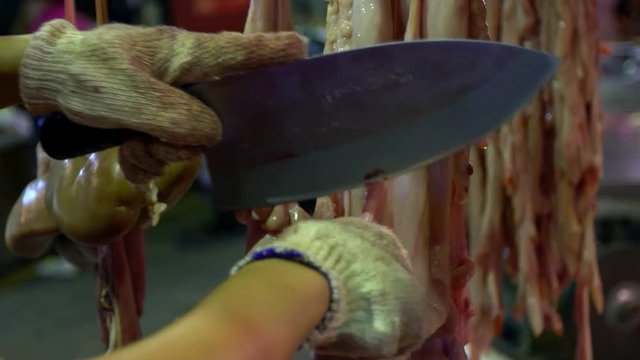 Slow motion of hands preparing raw organs pig hanging on hook for sale at traditional market. Stall vendor using knife while cutting pieces of pork. Taiwanese food selding in shop of marketplace-Dan