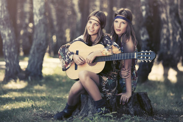 Two young fashion girls with guitar in a summer forest