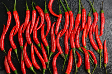 A lot of sharp hot spice red chilli cayenne pepper with wet drops of freshness water dew on a black graphite slate stone surface. Natural vegeterian diet organic vegetable. Dark food foto
