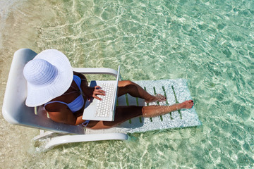 Woman resting on deck chair in turquoise water of white sand beach and using laptop.Copy space