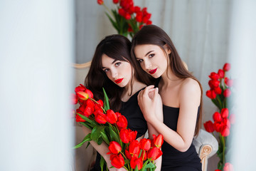 Fashion models in tender black dresses posing in sensual way at luxury interior full of tulips....