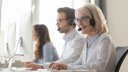 Smiling old female call center agent in headset consulting client