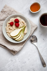oatmeal with raspberries and pear in a rustic plate on a marble table. Morning concept with copy space