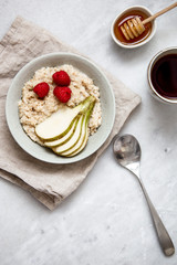 oatmeal with raspberries and pear in a rustic plate on a marble table. Morning concept with copy space