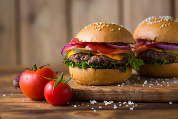 Classic american cheeseburger on a wooden board with tomatoes and onion.